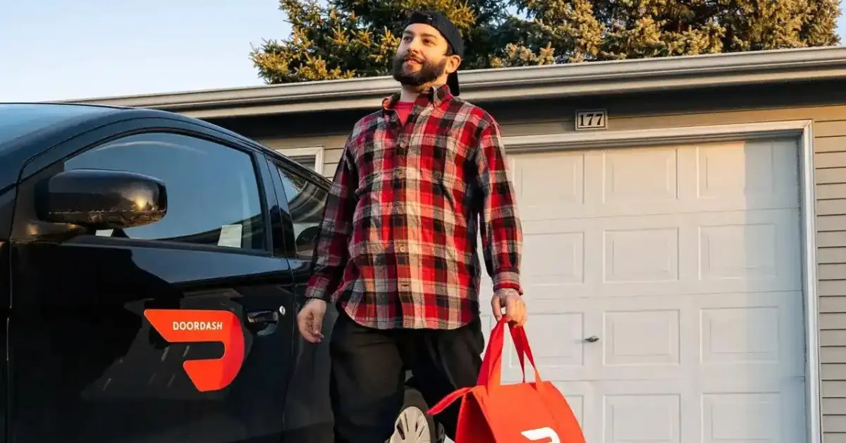 How Much Do DoorDash Drivers Make -- A standing man holding a bad of DoorDash