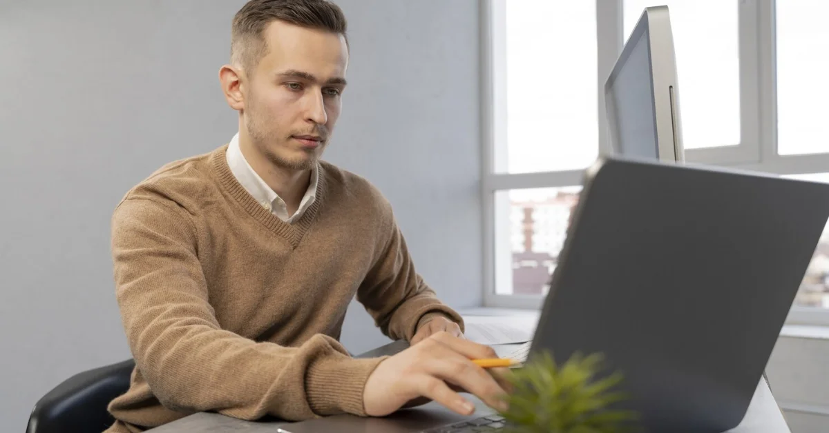 man using laptop while holding a pencil in his hand